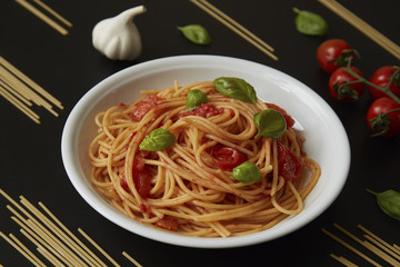 spaghetti dish with tomato sauce and basil on black background
