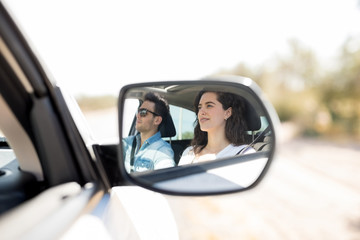 Reflection in side view mirror of couple traveling by car