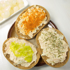 butter and tuna bread slices with spices and herbs on wooden board, decorated with onion, chilli and wasabi