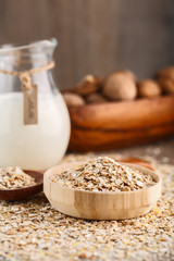 Dry rolled oatmeal in wooden bowl and wooden spoon on oatmeal background.