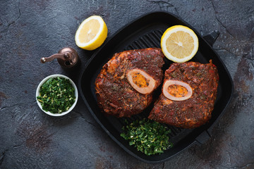 Cast-iron grill with raw marinated cross cut veal shanks for making ossobuco, top view on a weathered asphalt background