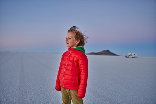 Young boy standing on salt flats, looking at view, recreational vehicle in background, Salar de Uyuni, Uyuni, Oruro, Bolivia, South America