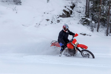 Motorcyclist on a crossover motorcycle rides in the snow. Turn of wheels a spray of snow