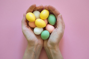 Colorful easter eggs in woman hands on pink background