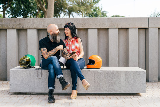 Tattooed mature hipster couple sitting on concrete bench