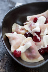Close-up of boiled vareniki or dumplings with cherries and sour cream, selective focus, vertical shot