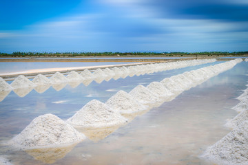 Sea salt fields with piled salt on blue sky background in Thailand.