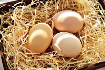 Three natural chicken eggs in a drawer with shavings in the backlight