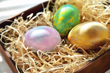 Fototapeta na wymiar Three colored chicken eggs in a box with shavings in the sunlight