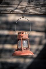 Red vintage kerosene lantern hanging in front of weathered wooden clap boards