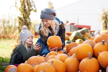 Young woman and daughter selecting pumpkin from stack at pumpkin patch