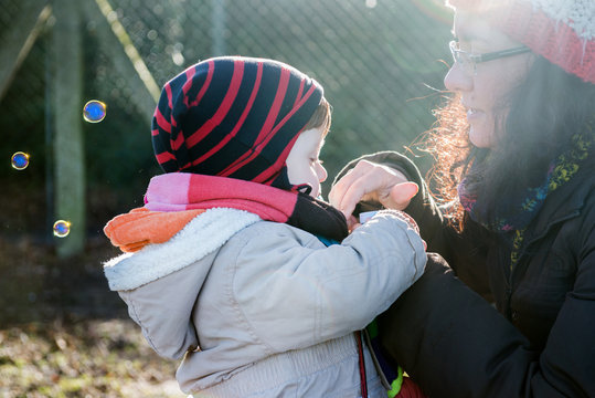 Male toddler and mother blowing bubbles in park