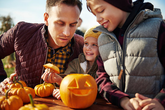 Man with son and daughter looking at carved halloween pumpkin at pumpkin patch