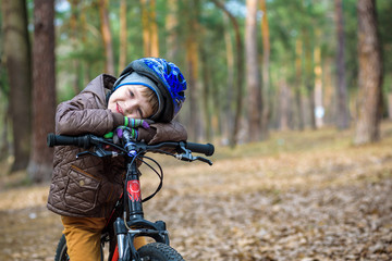 Fototapeta na wymiar Happy kid boy of 3 or 5 years having fun in autumn forest with a bicycle on beautiful fall day. Active child wearing bike helmet. Safety, sports, leisure with kids concept.