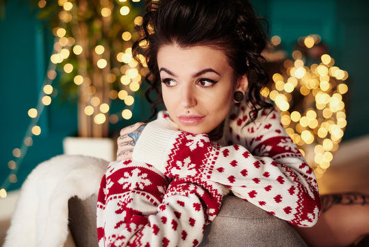 Young woman sitting at home, wearing christmas jumper, thoughtful expression