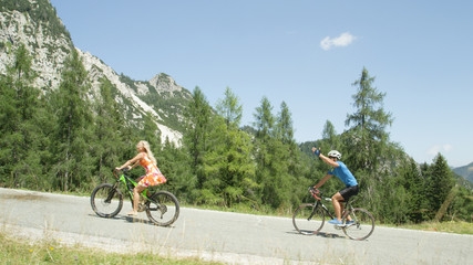 Naklejka premium Young blonde woman in pretty sundress pedals past pro bike rider on sunny day.