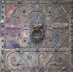 Elaborated door knocker lion head shaped on antique portal with bossed ornament and wrought iron decorations