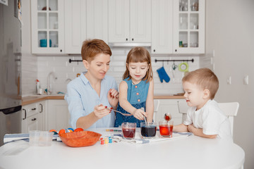 Mom and children, son and daughter paint their eggs with colors. Happy family is preparing for Easter.