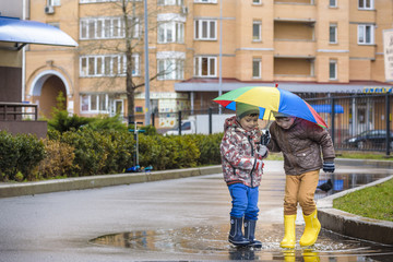 Two little boys, squat on a puddle, with little umbrellas