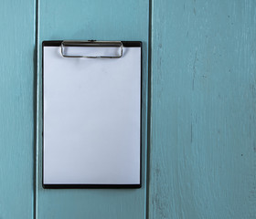 Clipboard with white sheet on wood background. Top view.Vintage style.