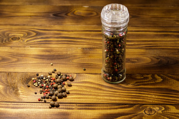 Glass pepper shaker with mix of peppercorn on wooden background
