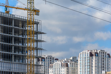 Construction site with crane and with unfinished skeleton of a high-rise building made of reinforced concrete against cloudy sky