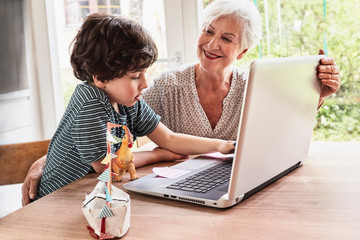 Grandmother and grandson sitting at table, using laptop