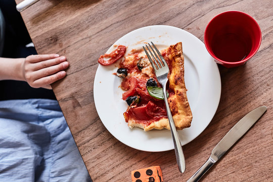 Slice Of Pizza On White Plate, Child's Hand On Table, Mid Section, Elevated View