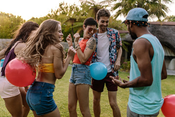 Group of friends playing balloon bursting game at party