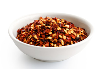 Coarsely ground chilli peppers in white ceramic bowl isolated on white.