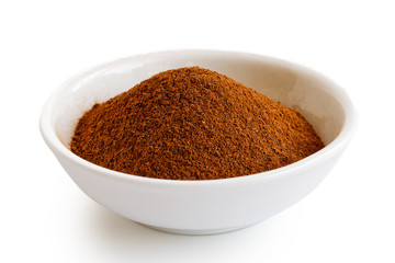 Finely ground cinnamon in white ceramic bowl isolated on white.