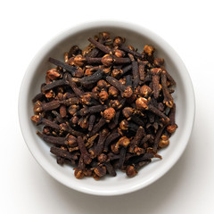 Whole cloves in white ceramic bowl isolated on white from above.