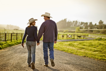 Happy husband and wife farmers walking hand in hand along a rural country road near their farm.