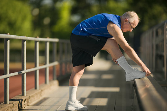 Senior man warming up with stretches on bleachers.