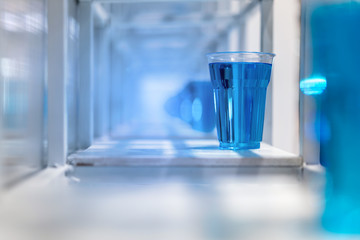 Blue water inside clear plastic cup on white metal shelf structure for decoration.