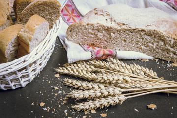 Fresh bread with and wheat on table close up. Sliced pieces of bread. Bread crumbs and fresh bread on the table. Rustic bread roll, wheat on black chalkboard. Rural kitchen or bakery.