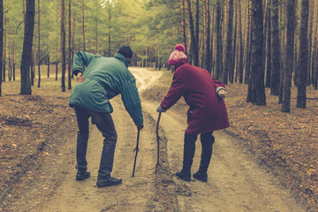 An elderly man and an elderly woman walking along a road in a pine forest