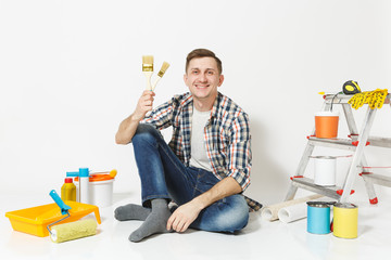 Smiling fun happy man sitting on floor with paint brush, instruments for renovation apartment room isolated on white background. Wallpaper, gluing accessories, painting tools. Repair home concept.