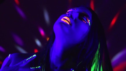 Fashion model girl with colorful fluorescent makeup in ultraviolet neon lights. Female disco dancer in UV light. Night club, party. 4K UHD video footage. 3840X2160