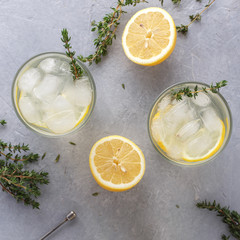 Cold lemonade with thyme in two glasses on the gray stone background.