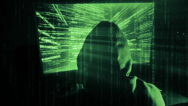 A man hacker in a hood in a dark room works with the program code