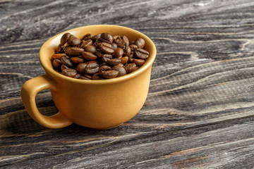 A coffee cup with coffee beans on an old wooden table. Fried coffee beans on a wooden background. Viewing from above.