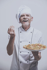 Senior male chief cook in uniform holding pizza on grey background