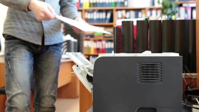White collar worker inserting paper in printer machine, close up view at device