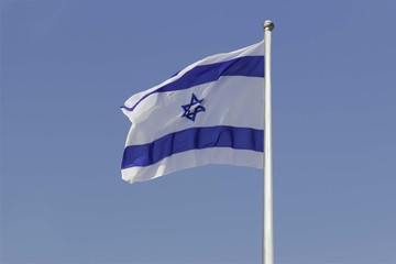 Israel flag flapping in the wind isolated against the blue sky. The flag is on a pole and flapping to the left. there are white clouds in the sky