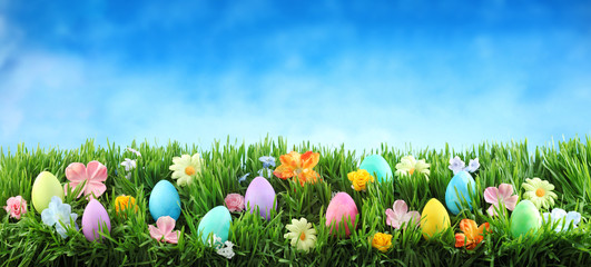 Bright colorful Easter eggs on green grass with flowers against blue sky