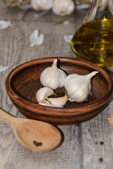 Garlic in a clay dish with a wooden spoon and olive oil on a table