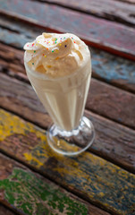 A colorfully  decorated Milkshake with lots og´f whipped Cream on a rustic Table made of painted Wood, shot from above