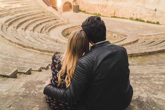 A couple embraces and shares a romantic moment while looking towards the stage of an ancient Greek theater. 