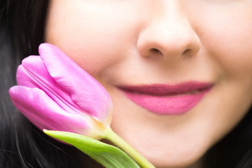 Nature or spring background. Young woman brunette with purple colored lips and purple tulip. Close up image with focus on the tulip. Valentines day or mothersday concept.